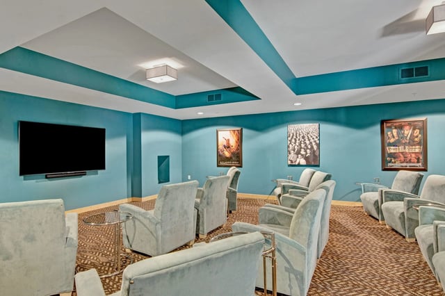 Teal-walled community theater room with cushioned chairs and a large wall-mounted screen.