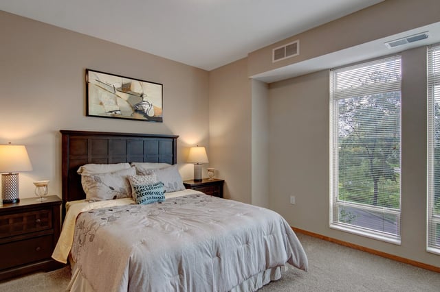 Bedroom interior with a dark wood headboard, two nightstands, lamps, and large window with blinds.