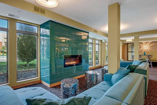Cozy communal lounge with a teal tiled gas fireplace, large windows, and blue sectional sofas.