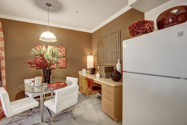 Dining area and workspace with a glass table, chairs, and a desk with a refrigerator.
