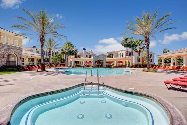 Resort-style swimming pool and spa area with lounge chairs and palm trees.