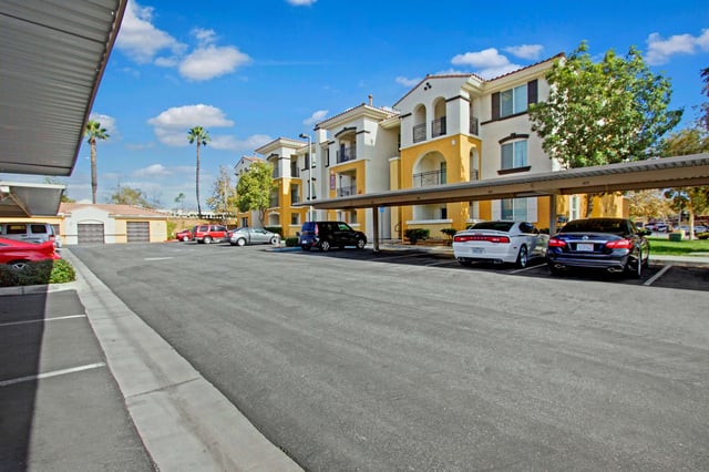 Apartment building exterior with covered parking and palm trees.