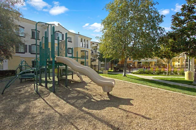 Playground equipment with slides and swings in front of apartment buildings.