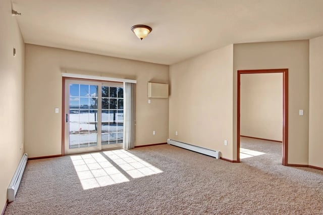 Empty living room with sliding glass door and entrance to another room.