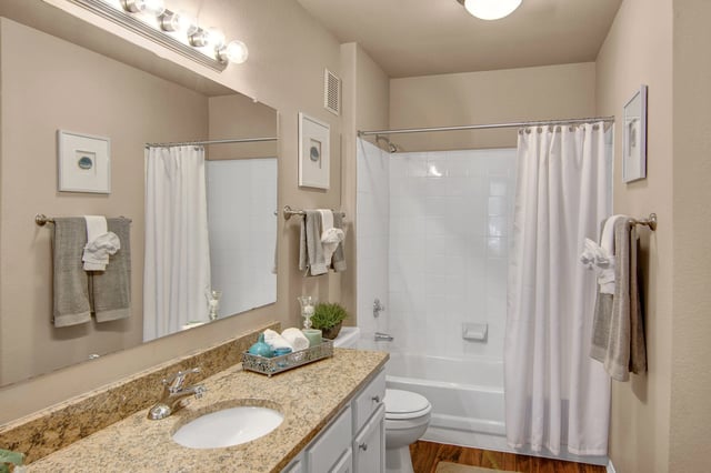 Bathroom with granite countertop vanity, white sink, and white tub with shower curtain.