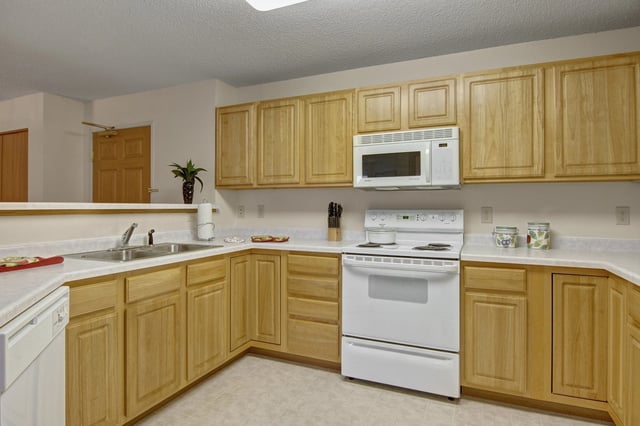 Kitchen with light wood cabinets, white countertops, a white stove and microwave.