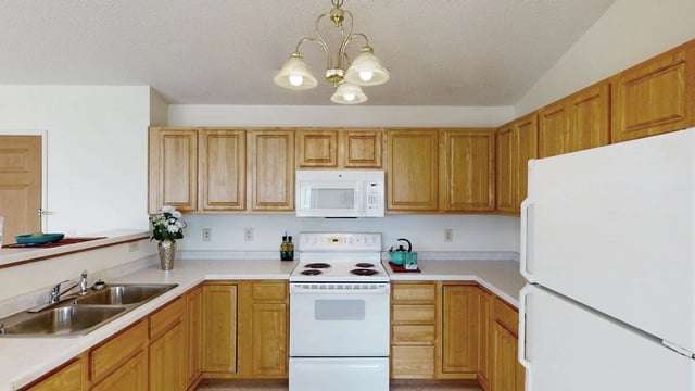 Kitchen with light wood cabinets, white countertops, and white appliances including a refrigerator, stove, and microwave.