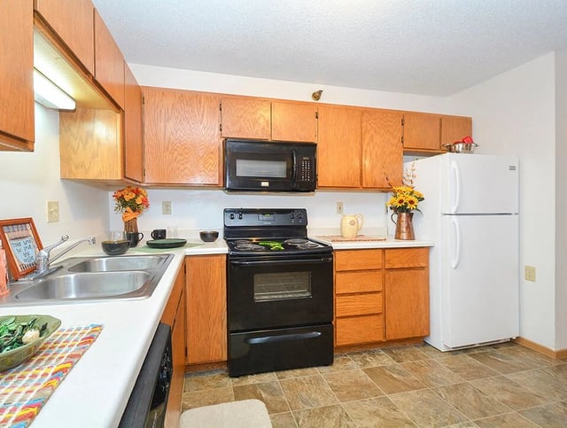 Kitchen with wooden cabinets, black appliances, and a white refrigerator.