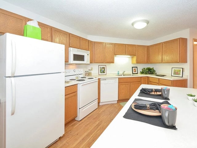 Kitchen with white appliances, wooden cabinets, and a breakfast bar.