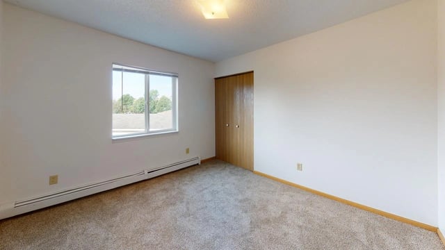 Interior view of a bedroom with a large window, closet, and carpeted floor.