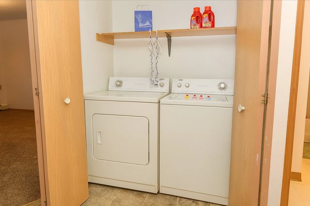 Stacked washer and dryer in a closet with wooden doors and a shelf above.