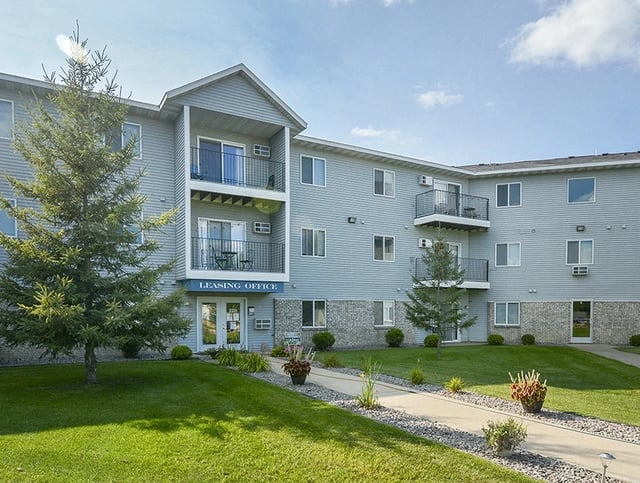 Exterior of apartment building with leasing office entrance and well-maintained landscaping.
