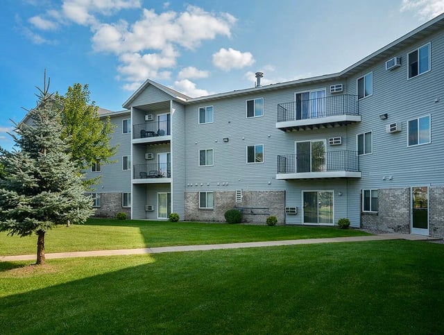 Exterior of a light gray apartment building with balconies and green lawn.