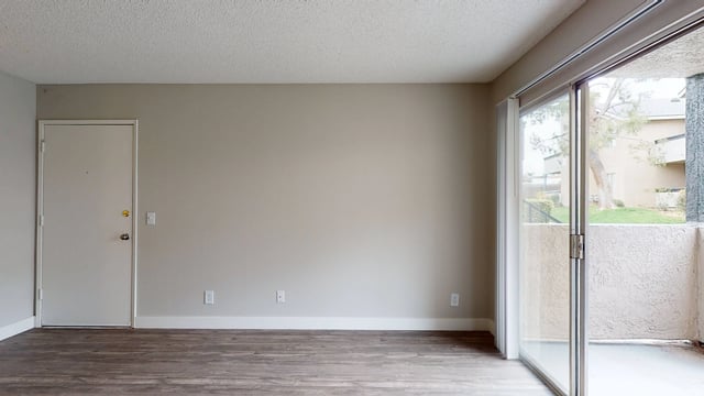 Empty apartment living room with a sliding glass door leading to a balcony.