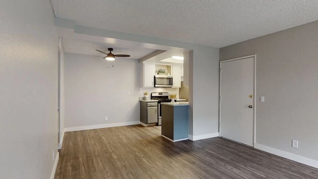 Kitchen and living area with wood floors, ceiling fan, and white door.