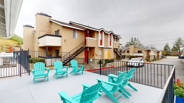 Apartment building exterior with teal Adirondack chairs on a patio and a pool area sign.