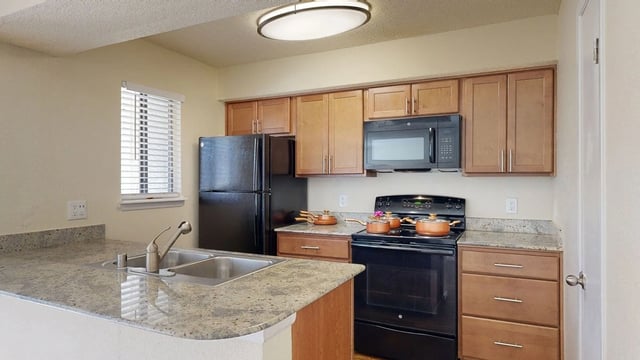 Modern kitchen with granite countertops, stainless steel sink, and black appliances.