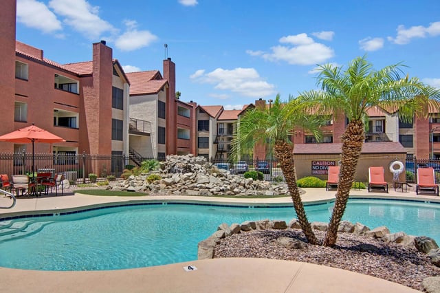 Resort-style swimming pool with lounge chairs and palm trees.