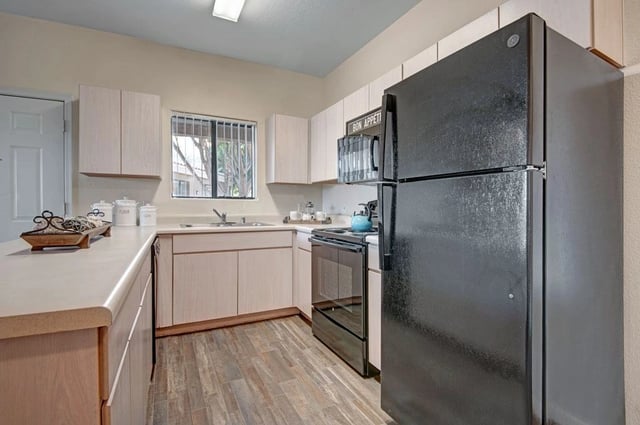 Kitchen with light wood cabinets, black appliances, and a window.