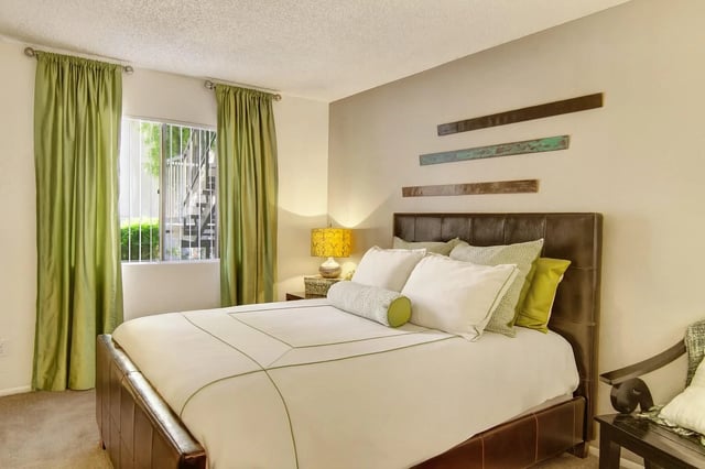 A modern bedroom with a queen-size bed, green curtains, and a bedside lamp.