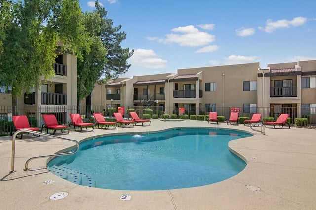Resort-style swimming pool with red lounge chairs and palm trees at an apartment complex.