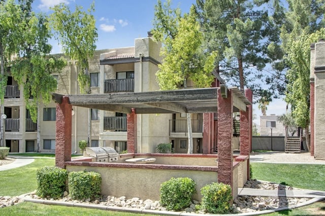 Outdoor grilling area with a pergola, built-in grill, and seating area, adjacent to apartment buildings.