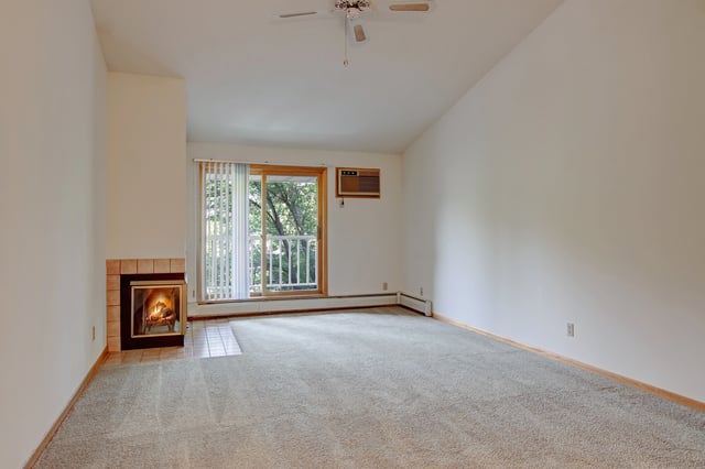Living room with fireplace, large carpeted floor space, and sliding glass door to balcony.