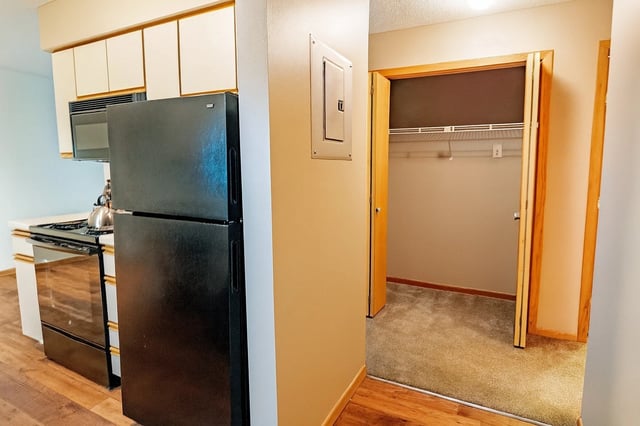 Kitchen with black refrigerator and stove, leading to a carpeted closet.
