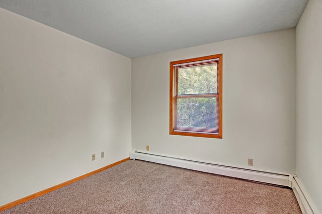 Empty bedroom with carpet, white walls, and a window with blinds.
