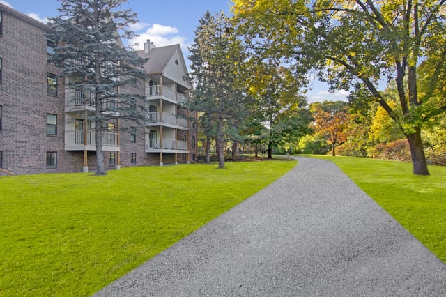 Brick apartment building with balconies surrounded by lush green lawns and mature trees.
