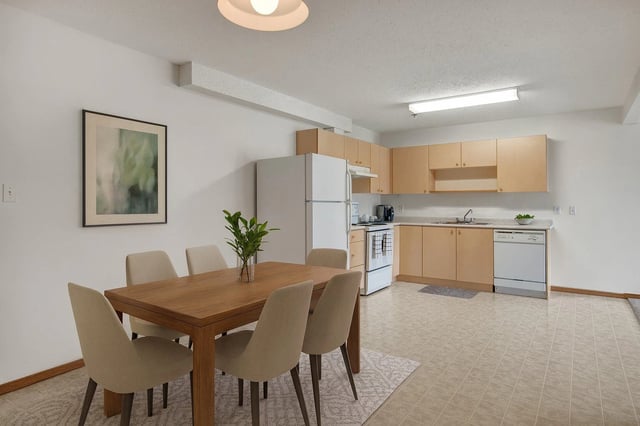 Dining area and kitchen with light wood cabinets, white appliances, and a wooden dining table with chairs.