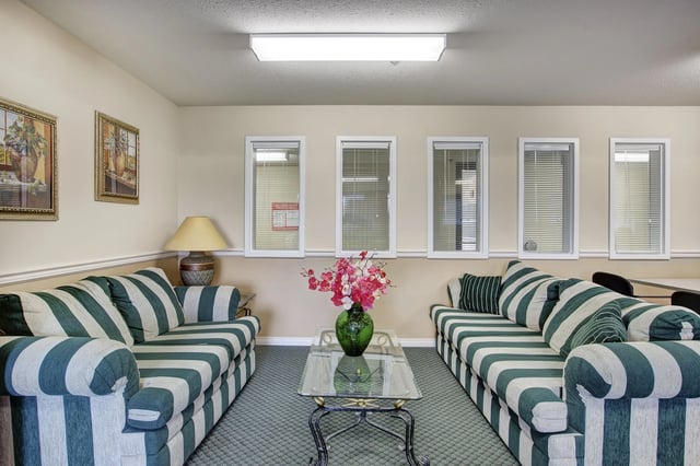 Community lounge area with two striped sofas, a glass coffee table with floral arrangement, and paintings on the wall.
