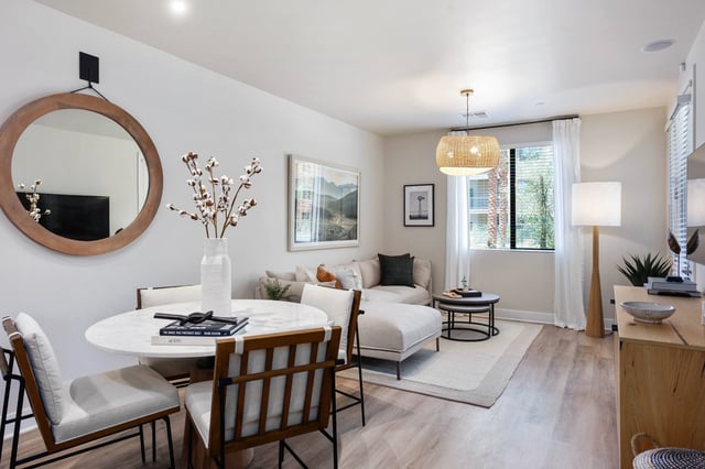 Dining area and living room with sectional sofa, large mirror, and natural light.