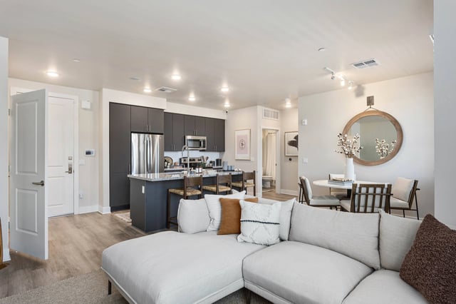 Modern living room and kitchen with sectional couch, island with bar stools, dining table, and stainless steel appliances.