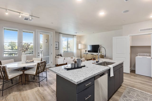 Modern kitchen and living area with island, dining table, sofa, and washer/dryer.