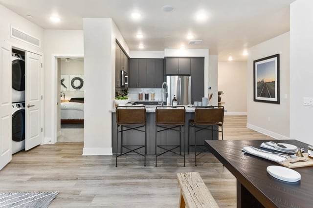 Modern kitchen with dark cabinets and stainless steel appliances, a granite island with bar stools, and a view of a bedroom.