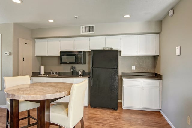 Kitchen area with a dining table, chairs, refrigerator, microwave, and cabinets.