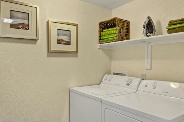 Washer and dryer set with framed beach art and decorative basket of towels.