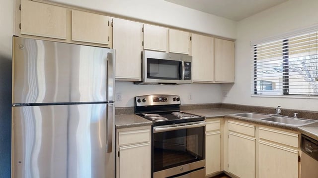 Stainless steel refrigerator, oven, and microwave in a bright apartment kitchen.