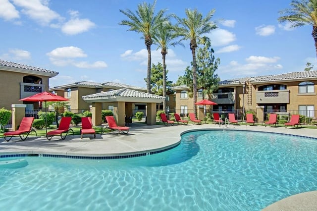 Resort-style swimming pool area with lounge chairs and palm trees.