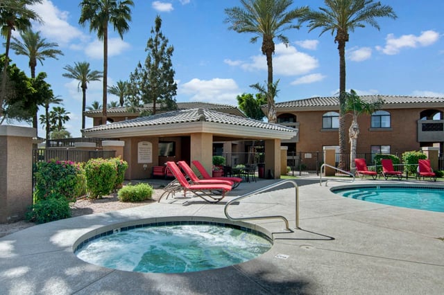 Outdoor swimming pool and jacuzzi with lounge chairs and palm trees.