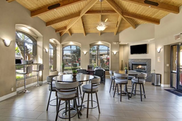 Community lounge area with high-top tables and chairs, fireplace, and large windows overlooking the pool.