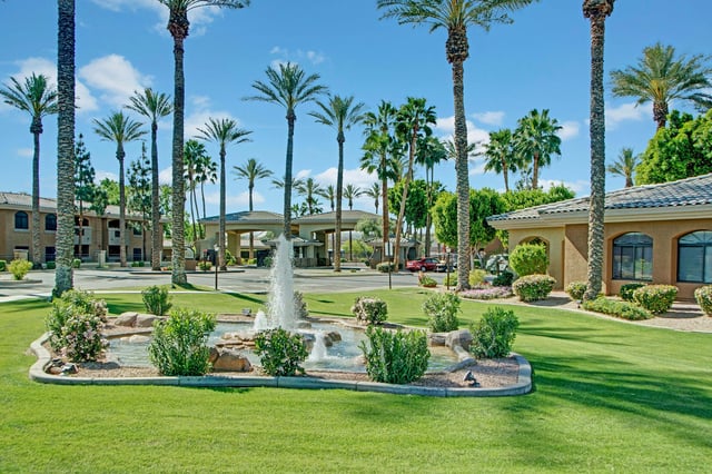 Property entrance with a water fountain and palm trees.