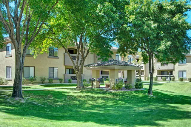 Apartment building exterior with trees and a covered picnic area with grills.