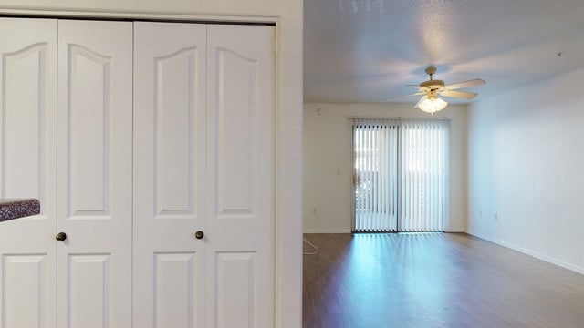 Closet doors and living room with ceiling fan and sliding glass door.