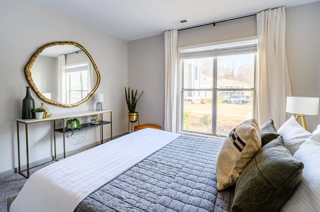 Bedroom with a large window, a golden abstract mirror, and a console table.
