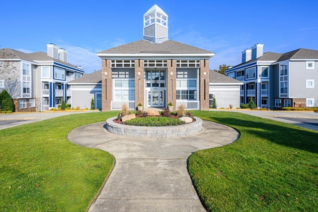 Exterior view of apartment buildings with manicured lawns and a circular flower bed in the foreground.