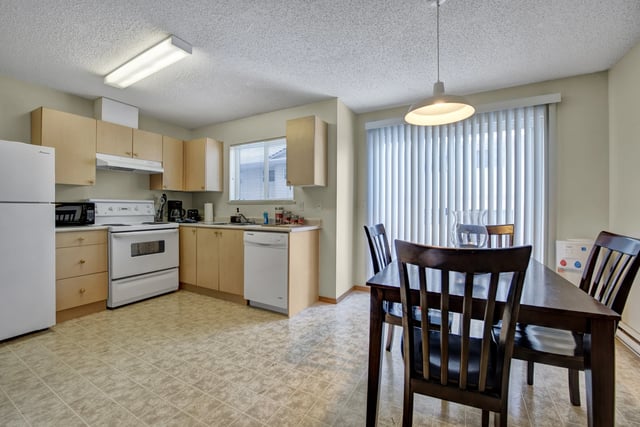 Kitchen and dining area with white appliances, light wood cabinets, and a dark wood dining table.