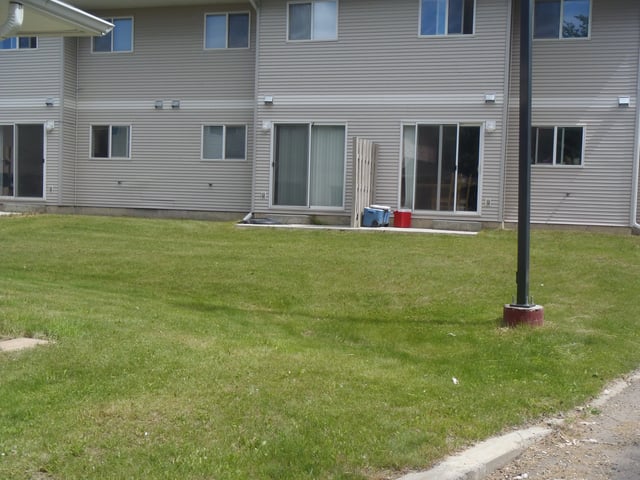 Exterior view of apartment building with grassy yard and pavement.