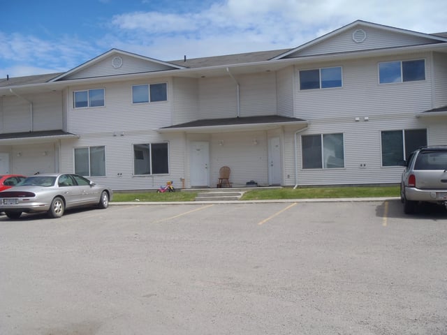 Exterior of a two-story apartment building with white siding, visible parking lot, and cars.
